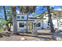 Bright modern home with a striking yellow door and unique stone accents and palm tree at 14016 Marguerite Dr, Madeira Beach, FL 33708