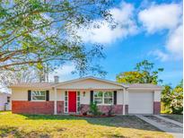 Brick ranch house with red door, attached garage, and well-manicured lawn at 4838 Longwood Ave, Holiday, FL 34690