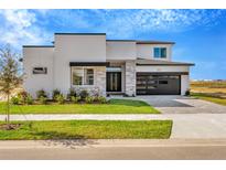 Two-story modern home with gray and white exterior, stone accents, and a black garage door at 32354 Wetland Bird Vw, San Antonio, FL 33576