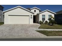 One-story home with light beige siding, a two-car garage, and a brick paver driveway at 6625 Pebblebrooke Way, Zephyrhills, FL 33541
