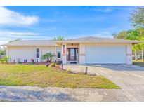 Tan house with a white garage door, landscaping, and a paved driveway at 2109 Elmwood Ct, Plant City, FL 33563