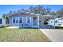 Gray mobile home with carport, landscaped lawn, and seating area at 4853 Blanco Dr, Zephyrhills, FL 33541