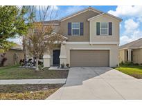 Two-story house with tan exterior, two-car garage, and landscaping at 1923 Broad Winged Hawk Dr, Ruskin, FL 33570