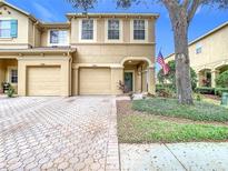 Tan two-story house with two-car garage, paver driveway, and American flag at 17523 Stinchar Dr # 17523, Land O Lakes, FL 34638