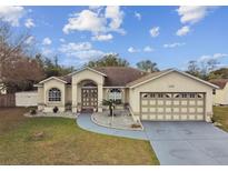 Tan house with a two-car garage and landscaped yard at 5136 Summer Hill Dr, Zephyrhills, FL 33542