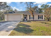 House exterior featuring a beige color, attached garage, and a well-maintained lawn at 12575 Maleo Rd, Weeki Wachee, FL 34614