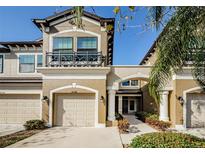 Tan three-story townhome with two-car garage, walkway, and landscaping at 11536 Crowned Sparrow Ln, Tampa, FL 33626