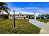 Ranch style home with carport, well-manicured lawn, and mature landscaping at 1205 Chevy Chase Dr, Sun City Center, FL 33573
