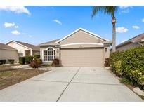 Tan house with two-car garage, landscaping, and palm tree at 2749 Plantain Dr, Holiday, FL 34691