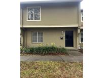 Tan two-story townhome with black door, landscaping, and sidewalk at 7638 Woodbridge Blvd, Tampa, FL 33615