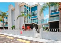 Condo building exterior, featuring a teal and white color scheme, gated entrance, and tropical landscaping at 343 Rex Pl # F, Madeira Beach, FL 33708