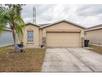 Beige house with a two-car garage and well-maintained lawn at 7962 Carriage Pointe Dr, Gibsonton, FL 33534