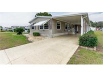 Tan mobile home with carport, landscaping, and paved driveway at 36900 Grace Ave, Zephyrhills, FL 33542