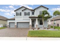 Two-story house with gray siding, stone accents, and a three-car garage at 13513 White Sapphire Rd, Riverview, FL 33579