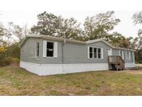 Gray manufactured home with white skirting, wooden steps, and surrounding trees at 12816 Midvale Ave, New Port Richey, FL 34654
