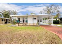 White single-wide mobile home with carport, landscaped lawn, and red driveway at 37318 Lois Ave, Zephyrhills, FL 33542