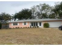 Ranch style home with pink exterior, mature landscaping, and a two-car garage at 3230 San Bernadino St, Clearwater, FL 33759