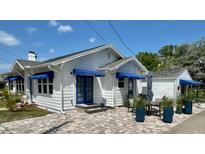 White house with blue awnings, landscaped yard, and brick paver patio at 410 W Lemon St, Tarpon Springs, FL 34689