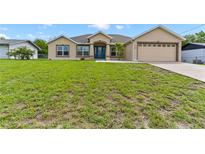 Tan house with blue door, attached garage, and large grassy yard at 4522 Gondolier Rd, Spring Hill, FL 34609