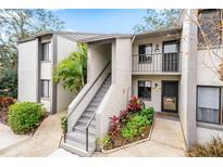 Two story condo building with gray siding, stairs, and lush landscaping at 2375 Lake Heather Heights Ct # 202, Dunedin, FL 34698