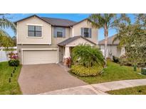 Two-story house with a tan exterior, brick driveway, and lush landscaping at 13355 Orca Sound Dr, Riverview, FL 33579