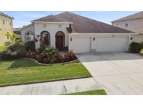 House exterior featuring a two-car garage, manicured lawn, and attractive landscaping at 18442 New London Ave, Land O Lakes, FL 34638