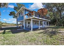 Elevated blue home with deck, carport, and surrounding lush landscaping at 10581 Pine Island Dr, Weeki Wachee, FL 34607