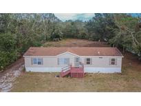 Tan mobile home with wooden deck, situated on a grassy lot with mature trees at 12914 Gordon Rd, Riverview, FL 33579