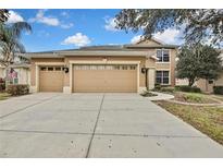 Two-story house with beige exterior, three-car garage, and landscaped yard at 4381 Caliquen Dr, Brooksville, FL 34604