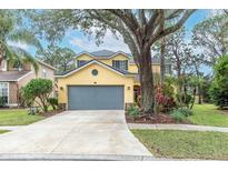 Two-story yellow house with gray garage door, landscaping, and a large tree in the front yard at 5608 Rockfield Loop, Valrico, FL 33596