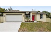 Newly constructed home with a red door, attached garage, and well-manicured lawn at 15958 Adobe Dr, Hudson, FL 34667