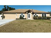 Tan house with a brown roof, attached garage, and landscaped yard at 1447 Coble Rd, Spring Hill, FL 34608