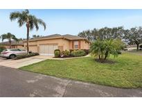 Tan single-story home with attached garage, landscaping, and palm trees at 2028 Acadia Greens Dr, Sun City Center, FL 33573