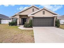 Beige house with dark gray garage door, landscaping, and a walkway at 11521 Sunder Berry St, Hudson, FL 34667