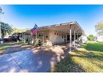 Tan single-wide home with carport, American flag, and mature trees at 37025 Karen Ave, Zephyrhills, FL 33542