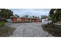 Orange single story home with a large driveway and mature landscaping at 7063 S Shore S Dr, St Petersburg, FL 33707