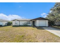 Ranch-style home with a white exterior, attached garage, and mature lawn at 7310 Oakshire Dr, Port Richey, FL 34668