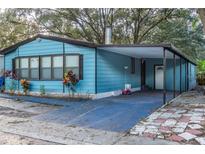 Light blue single-wide mobile home with carport and landscaped yard at 10559 Bay Hills Cir, Thonotosassa, FL 33592
