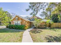 Tan house with green landscaping, walkway, and fenced backyard at 2920 Longbrooke Way, Clearwater, FL 33760