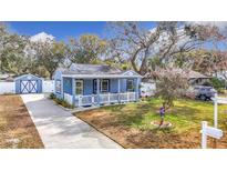 Charming blue house with a white picket fence, landscaping, and a long driveway at 1447 Santa Anna Dr, Dunedin, FL 34698