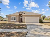 Tan one-story house with a two-car garage and well-manicured lawn at 2309 Cross Tee Ct, Brooksville, FL 34604