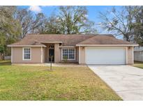Beige house with brown roof, white garage door, and landscaped lawn at 5332 Nutcracker Cir, Land O Lakes, FL 34639