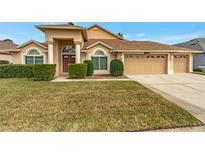Tan house with three-car garage, lush lawn, and manicured hedges at 10025 Cypress Shadow Ave, Tampa, FL 33647