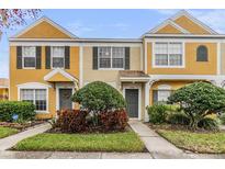 Two-story townhome with yellow siding, landscaping, and a gray door at 1308 Costa Mesa Dr, Wesley Chapel, FL 33543