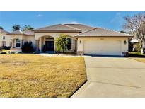 One-story house with a large yard, two-car garage, and palm tree at 9445 Southern Belle Dr, Weeki Wachee, FL 34613