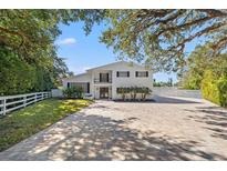 Two-story home with a brick paver driveway and a white picket fence at 1 Gallinule Pl, Belleair, FL 33756