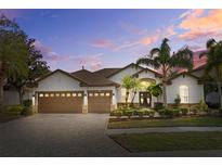 Beautiful home featuring a three-car garage, lush landscaping, and a paver driveway at 1893 Riveredge Dr, Tarpon Springs, FL 34689