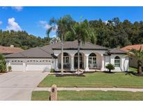 White house with dark brown roof, 3-car garage, and lush landscaping at 1257 Kings Way Ln, Tarpon Springs, FL 34688