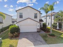 Beautiful two-story home featuring a brick driveway, a two-car garage, and a green lawn with palm trees at 12408 Victarra Pl, New Port Richey, FL 34655