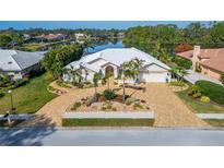 Stunning waterfront home featuring lush landscaping, a brick driveway, and a pristine white tile roof at 7566 Links Ct, Sarasota, FL 34243